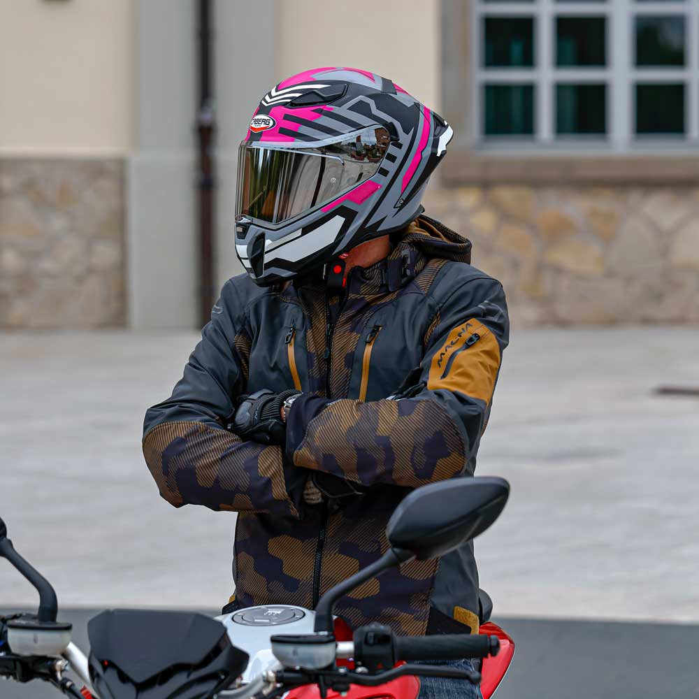 biker wearing brown and black motorcycle jacket for men with black and pink motorbike helmet next to a motorcycle