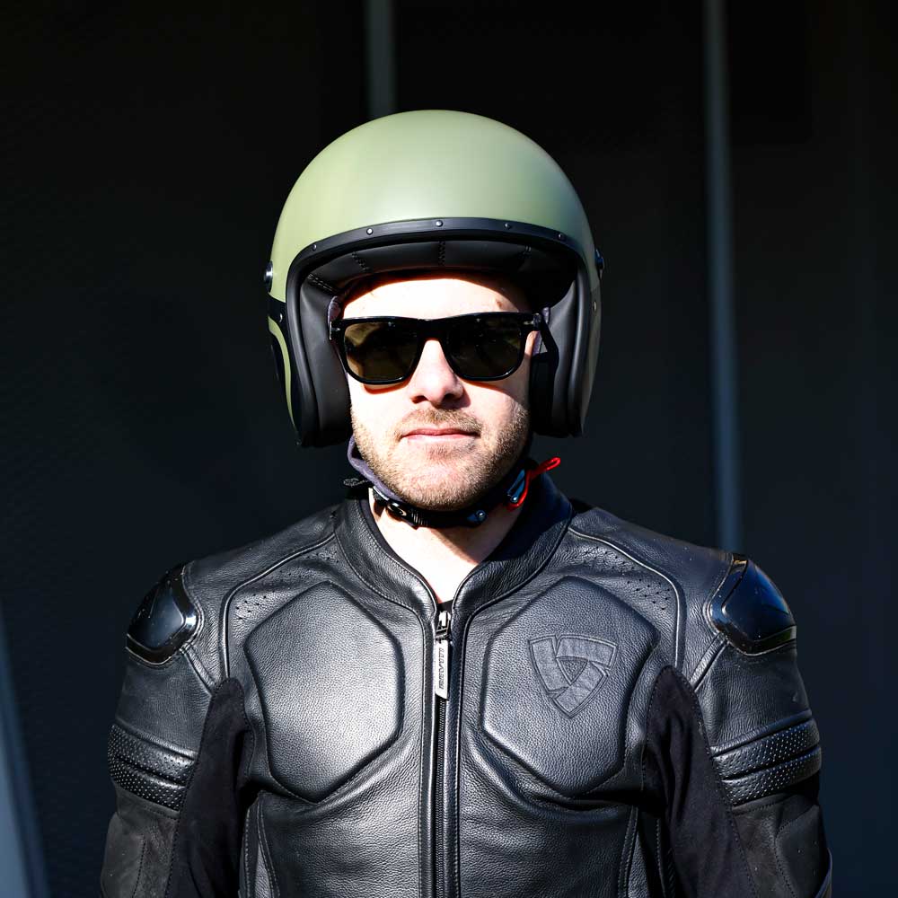 front of biker wearing black race suit with matte military green and black motorbike helmet
