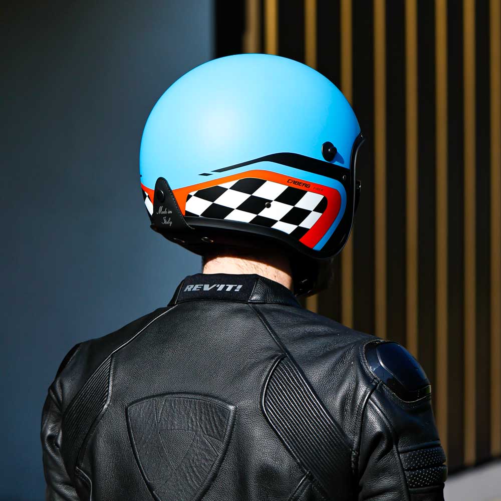 back of biker wearing matte blue and orange open face helmet with black and white chequered design