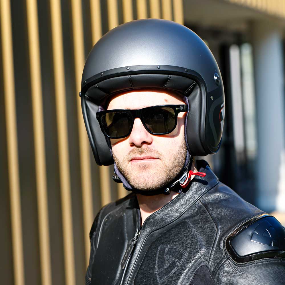 biker wearing black race suit with black open face motorbike helmet and shades