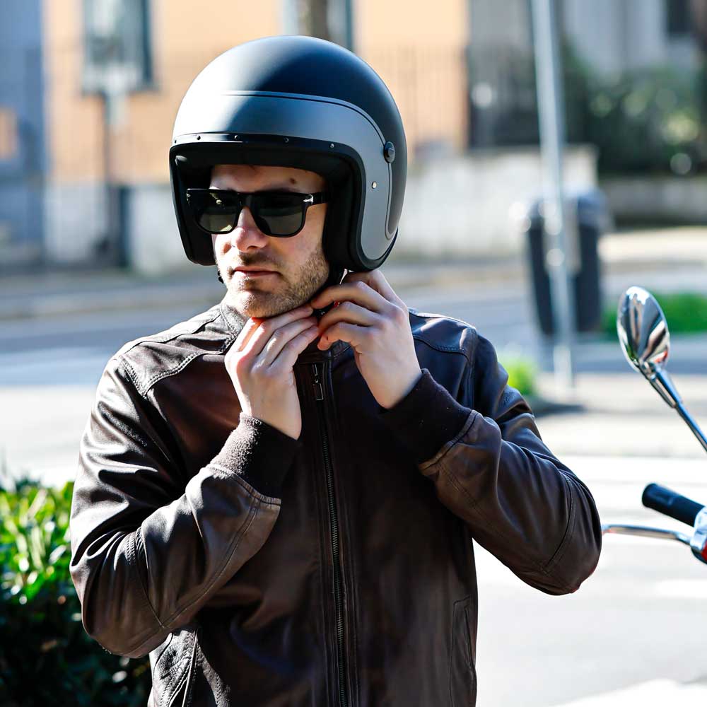 biker strapping on his chin strap of matte black motorcycle helmet with open face design