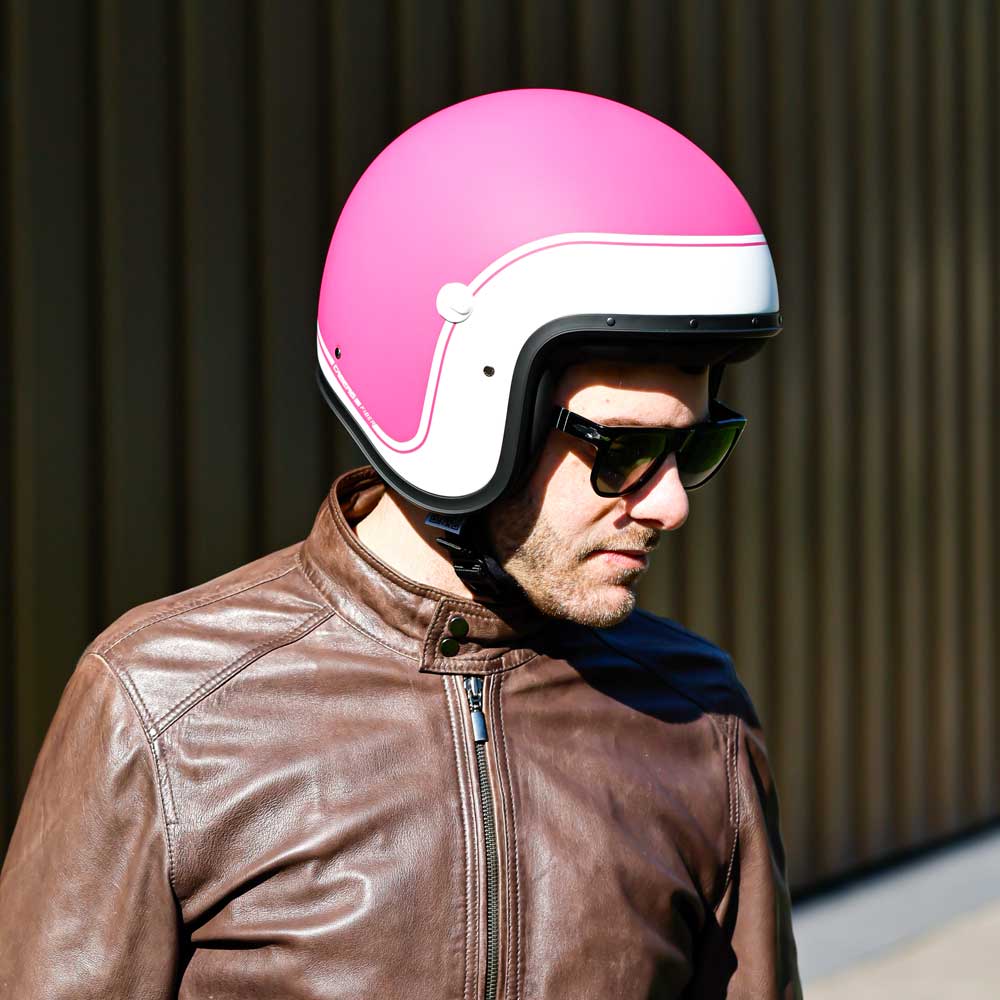 side of biker wearing fuchsia pink open face motorbike helmet with white border around the edge