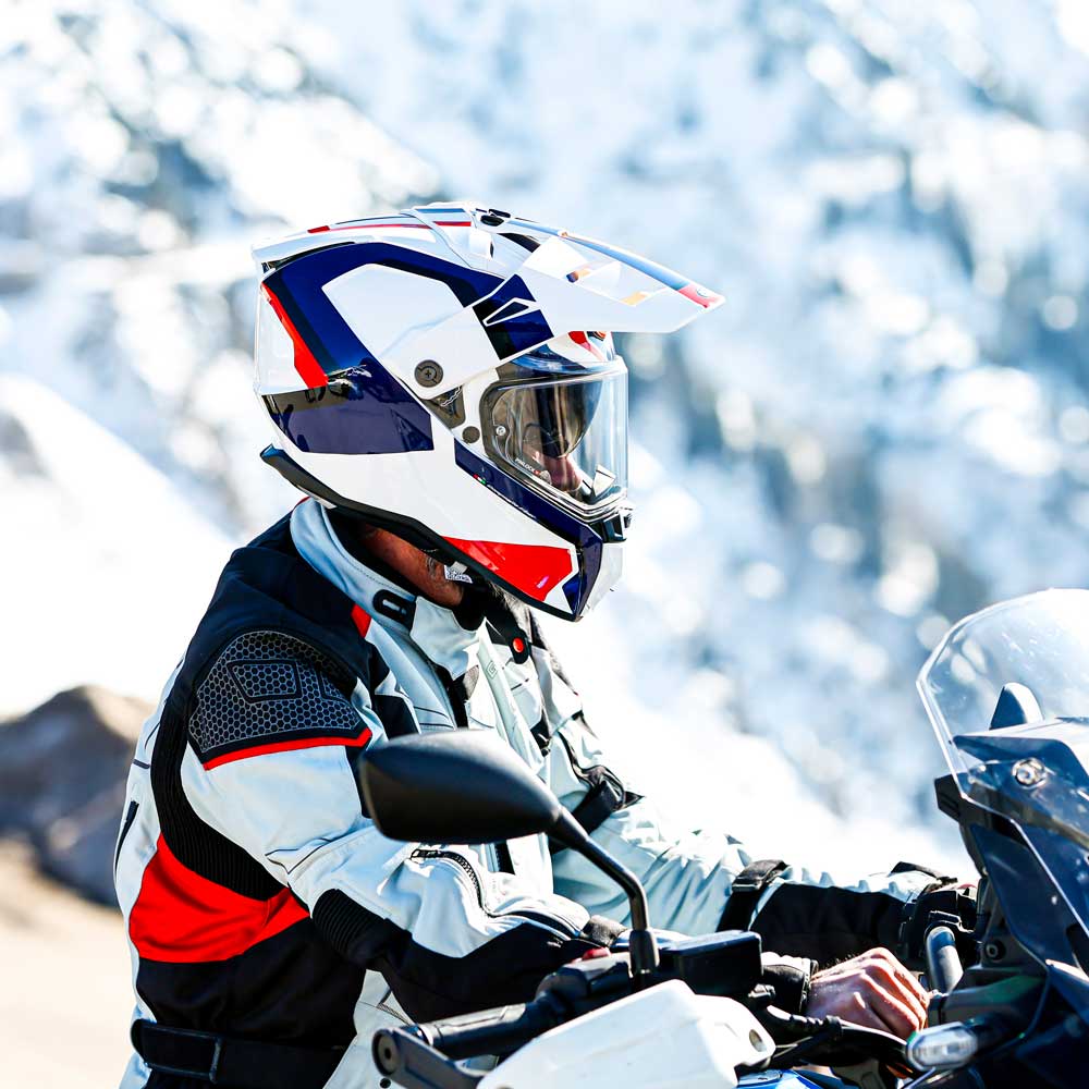 biker sitting on motorcycle wearing white and red motorbike gear and helmet in the mountains
