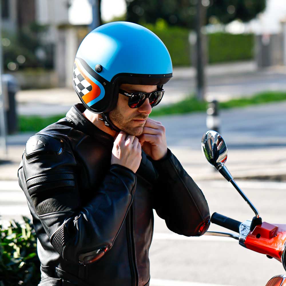 biker strapping on the caberg freeride x blue and orange motorbike helmet with white and black chequered design
