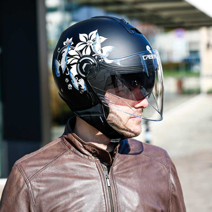 A man looking left while wearing the helmet, with both visors down, displaying the clean helmet lines and side floral detailing.